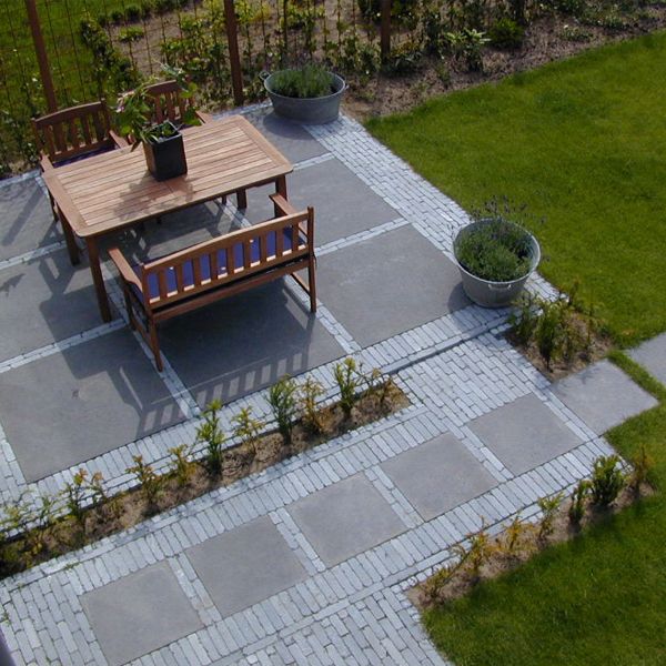 Bestraat terras in grijze natuursteentegels gecombineerd met kleine klinkers, met houten tuinset en lavendel langs het gazon
